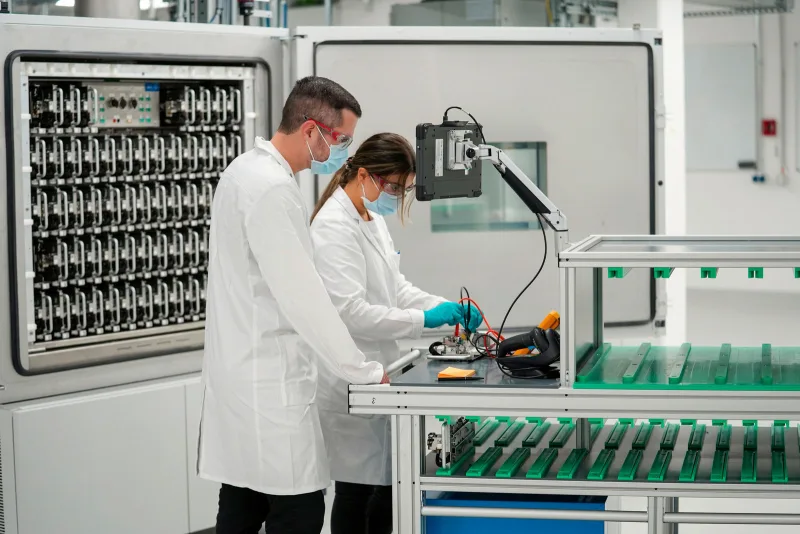 Deux techniciens en blouse blanche travaillant sur une batterie dans un laboratoire d'essais