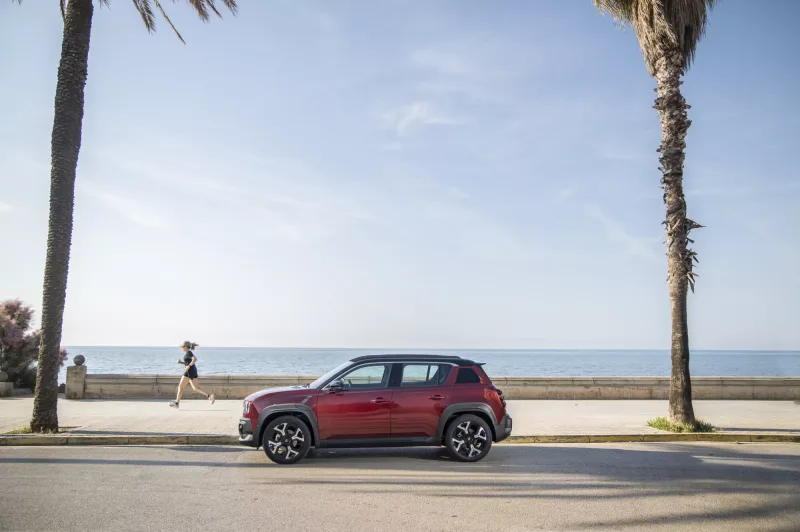 Renault 4 E-Tech electric Plein Sud rouge de profil le long d'une promenade en bord de mer