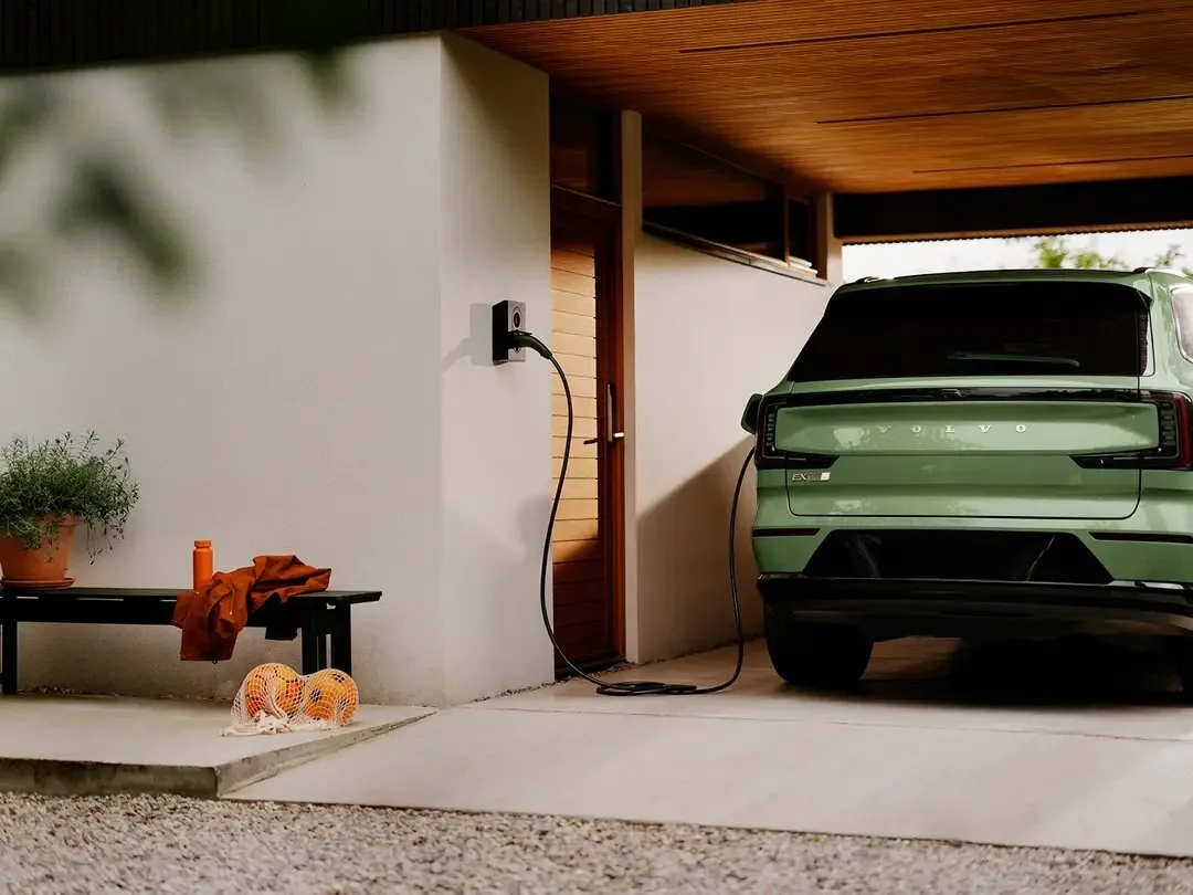 Borne Zaptec Go 2 fixée au mur d'un abri voiture, câble branché sur un SUV électrique vert