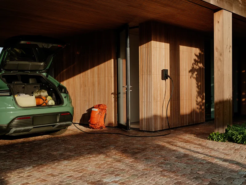 Borne Zaptec Go fixée au mur d'une maison en bois, câble branché sur une voiture électrique