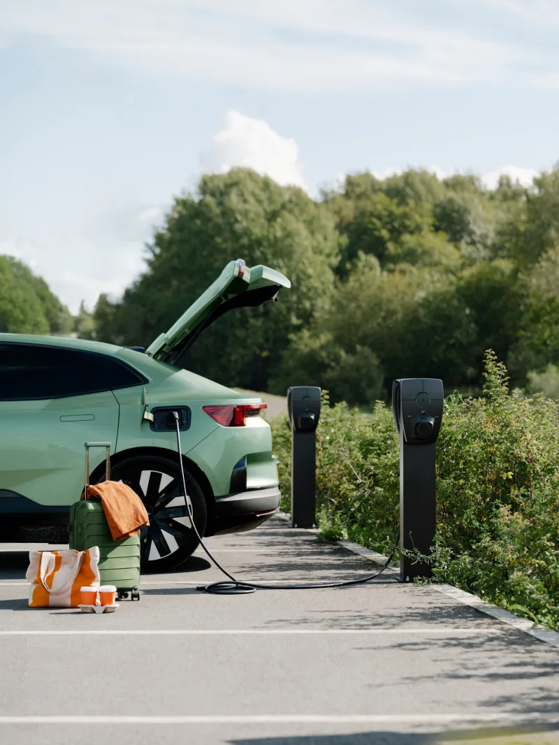 Voiture électrique verte garée devant deux bornes de recharge sur pied, hayon ouvert