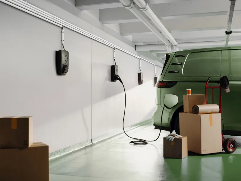 Plusieurs bornes murales Zaptec alignées dans un garage, câble noir branché sur une camionnette électrique verte