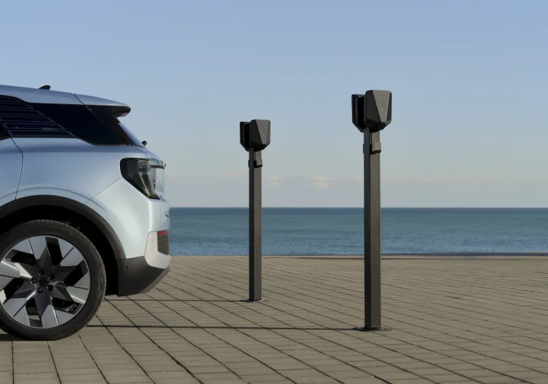Deux bornes de recharge Easee sur pied à côté d'une voiture électrique grise, devant la mer