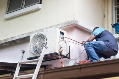 Technicien raccordant les tuyaux en cuivre d'une unité extérieure de climatisation fixée au mur d'un immeuble