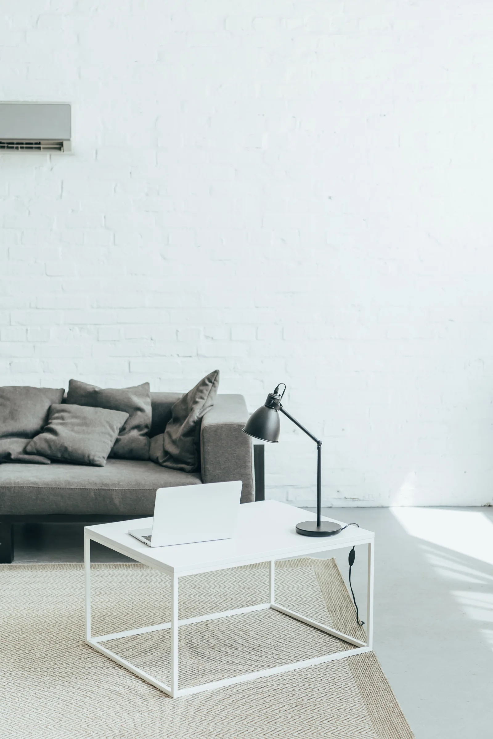 Salon lumineux avec canapé gris, table basse blanche et climatiseur mural au-dessus