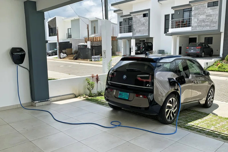 BMW i3 vue de l'arrière, câble de recharge tendu jusqu'à une borne murale